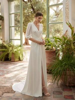Robe de mariée fourreau toute simple en crêpe. Ce modèle délicat signé Alma Novia présente un décolleté en V, un dos en goutte d'eau, des manches trois-quarts et une jupe fendue sur le devant.